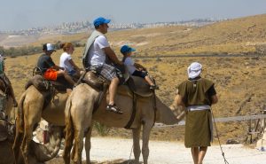 A staff member portraying Eliezer (far right) assists visitors in mounting their camels as they prepare to travel to Avraham’s tent.