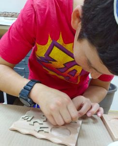 A young boy at The Workshop glues letters onto the base of his candle holder. Photos courtesy of Mandy Broder